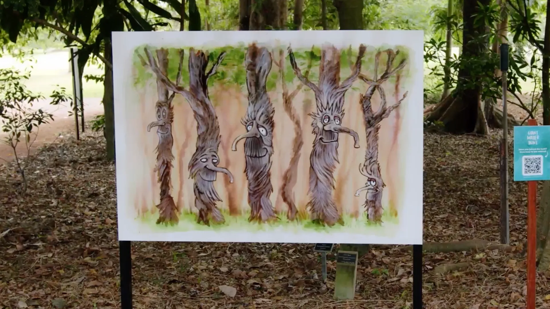 Giant Water Hunt - painted AR marker board of tree characters with faces, mounted on a Townsville bushland trail beside a QR code sign